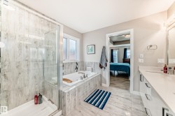Modern bathroom featuring a glass-enclosed shower with large format tile, a built-in tub with tile surround, and a vanity with a white countertop and integrated sink - 