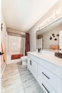 Bright bathroom featuring a large vanity with white cabinetry and dark hardware, a white countertop, and a wide mirror with overhead lighting - 