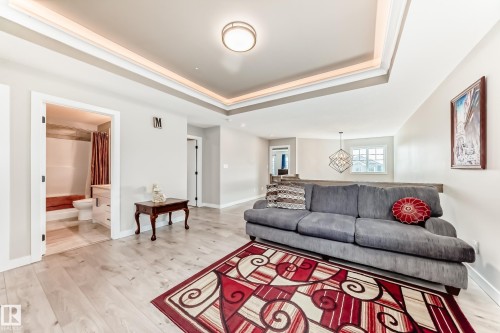 Open-concept living space featuring light wood-finish flooring, a tray ceiling with integrated lighting, and a modern flush-mount light fixture - 3895 Robins Crescent, Edmonton, AB 