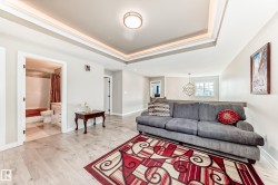 Open-concept living space featuring light wood-finish flooring, a tray ceiling with integrated lighting, and a modern flush-mount light fixture - 