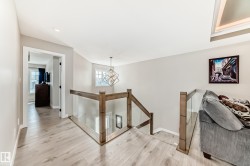 Open hallway featuring wood-finish flooring, a contemporary glass and wood railing, recessed lighting, and a geometric chandelier - 