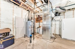 Basement utility area featuring a water heater, furnace, and exposed ceiling joists with wiring and plumbing - 