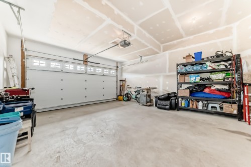 Spacious garage featuring a sectional overhead door with window inserts, exposed ceiling joists, and concrete flooring - 3895 Robins Crescent, Edmonton, AB 