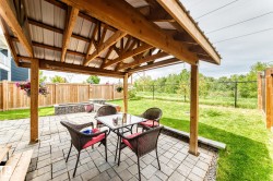 Covered outdoor patio featuring a wood-frame gazebo with a metal roof, paver flooring, a stone-faced planter box, and a wood privacy fence - 