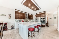 Bright kitchen featuring an expansive center island with a white countertop, dark wood-finish cabinetry, stainless steel appliances, a mosaic tile backsplash, and light wood-finish flooring - 
