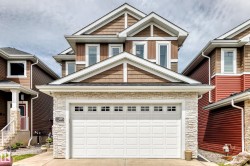 Contemporary exterior featuring brown siding, textured cedar shake accents, white trim, stone veneer detailing, and a prominent garage with paneling and window inserts - 