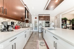 Open-concept kitchen featuring an elongated central island with an undermount double sink, stainless steel appliances, two-tone cabinetry, mosaic tile backsplash, and recessed lighting - 