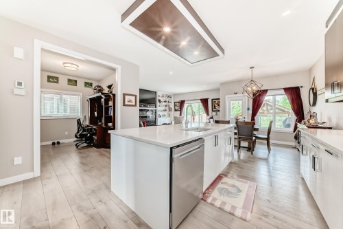 Contemporary kitchen featuring a large center island with integrated sink, stainless steel dishwasher, and light-toned countertops - 3895 Robins Crescent, Edmonton, AB 
