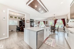 Contemporary kitchen featuring a large center island with integrated sink, stainless steel dishwasher, and light-toned countertops - 