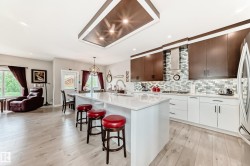 Open-concept kitchen featuring an expansive island with a white quartz countertop, two-tone cabinetry, a mosaic tile backsplash, and light wood-finish flooring - 