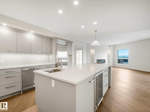 Contemporary kitchen featuring an oversized island with an under-counter beverage cooler, stainless steel appliances, light-toned cabinetry, and wood-finish flooring - 902 10108 125 Street, Edmonton, AB 