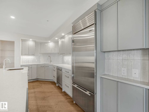Modern kitchen featuring a stainless steel refrigerator, white cabinetry, light wood-finish flooring, and recessed lighting - 902 10108 125 Street, Edmonton, AB 