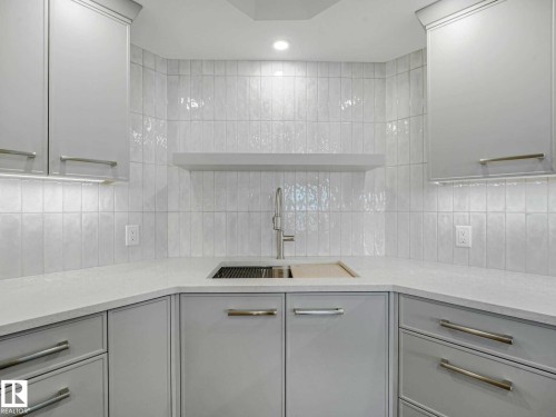 Kitchenette featuring a stainless steel sink with a high-arc faucet, light gray cabinetry, white countertops, and vertical subway tile backsplash - 902 10108 125 Street, Edmonton, AB 