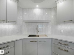 Kitchenette featuring a stainless steel sink with a high-arc faucet, light gray cabinetry, white countertops, and vertical subway tile backsplash - 