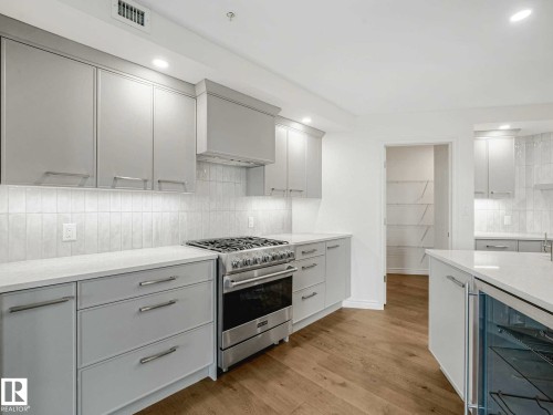 Modern kitchen featuring light gray cabinetry, stainless steel range, white countertops, tile backsplash, and light wood-finish flooring - 902 10108 125 Street, Edmonton, AB 