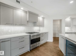 Modern kitchen featuring light gray cabinetry, stainless steel range, white countertops, tile backsplash, and light wood-finish flooring - 