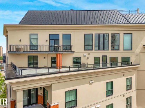 Contemporary building exterior featuring a metal roof, stucco facade, multiple balconies with metal railings, a spacious rooftop patio with glass railings, and expansive windows - 902 10108 125 Street, Edmonton, AB 
