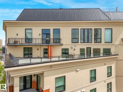 Contemporary building exterior featuring a metal roof, stucco facade, multiple balconies with metal railings, a spacious rooftop patio with glass railings, and expansive windows - 