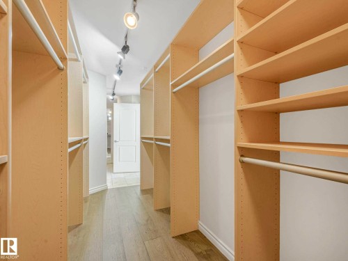 Spacious walk-in closet featuring extensive built-in shelving, multiple hanging rods, and wood-finish flooring - 902 10108 125 Street, Edmonton, AB 