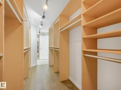 Spacious walk-in closet featuring extensive built-in shelving, multiple hanging rods, and wood-finish flooring - 