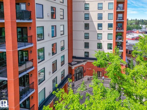 Multi-story residential building featuring a brick and stucco facade, multiple private balconies with black railings, and an arched entryway - 902 10108 125 Street, Edmonton, AB 