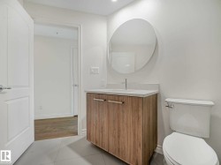 Contemporary vanity featuring a light wood-finish cabinet with sleek hardware, a white countertop, and a circular wall-mounted mirror - 