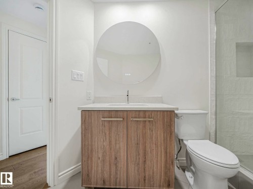 Bathroom vanity featuring a wood-finish cabinet, white countertop, and circular mirror - 902 10108 125 Street, Edmonton, AB 