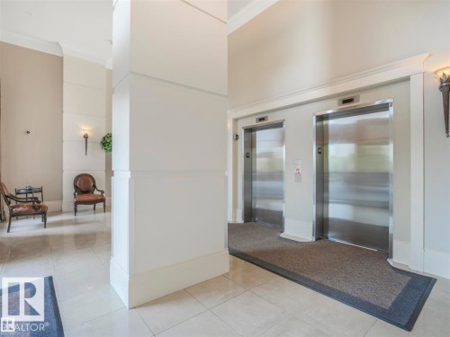 Brightly lit hallway featuring two stainless steel elevators, light-toned tile flooring, white trim work, and sconce lighting - 902 10108 125 Street, Edmonton, AB 