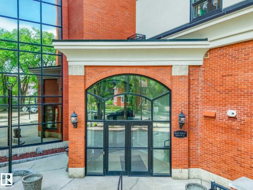 Brick building exterior featuring a prominent arched glass entryway with transom window, full-light double doors, two wall-mounted outdoor light fixtures, and a large multi-story window wall - 902 10108 125 Street, Edmonton, AB 