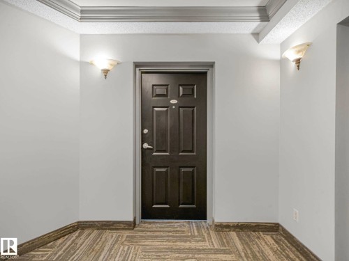 Entryway featuring a paneled door, decorative wall sconces, crown molding, and patterned carpet - 902 10108 125 Street, Edmonton, AB 