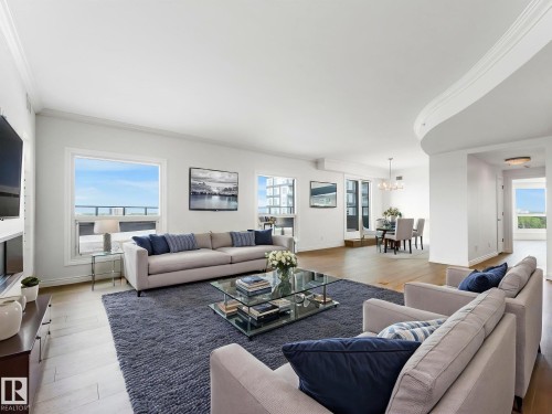 Open-concept living area featuring light wood-finish flooring, white crown molding, large picture windows, and a dedicated dining space with a chandelier - 902 10108 125 Street, Edmonton, AB 