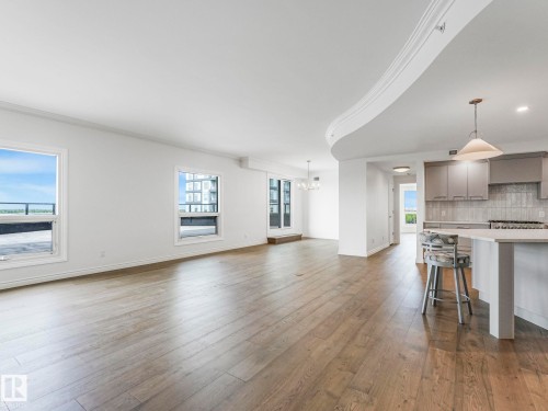 Spacious open-concept living area featuring wood-finish flooring, multiple windows, recessed lighting, and crown molding - 902 10108 125 Street, Edmonton, AB 