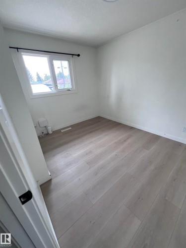 Light-filled room featuring wood-finish flooring, white walls, and a window with a black curtain rod - 11911 133 Avenue, Edmonton, AB 