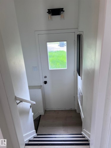 Entryway featuring a white door with an integrated window, wood-finish flooring, a wall-mounted light fixture, and stairs with contrasting treads - 11911 133 Avenue, Edmonton, AB 