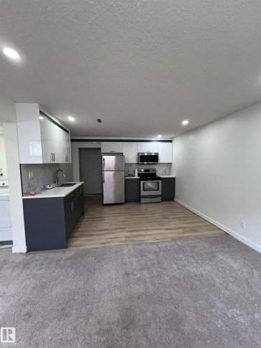 Contemporary kitchen featuring two-tone cabinetry with stainless steel hardware, stainless steel appliances, a white countertop, and a coordinating backsplash - 11911 133 Avenue, Edmonton, AB 