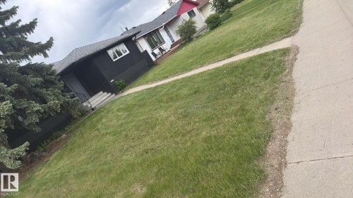 Front yard with established evergreen landscaping, concrete walkway, and paved sidewalk - 11911 133 Avenue, Edmonton, AB 