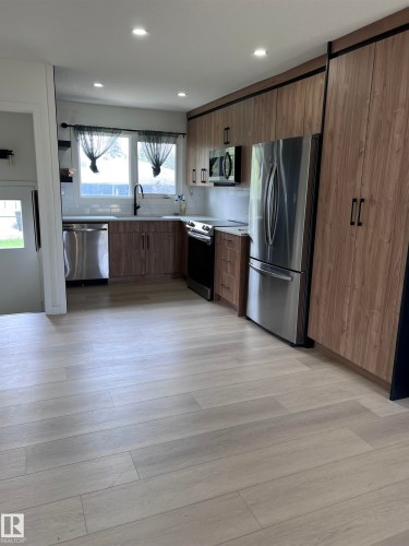 Contemporary kitchen featuring wood-finish cabinetry, stainless steel appliances, a white subway tile backsplash, and light wood-finish flooring - 11911 133 Avenue, Edmonton, AB 