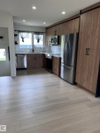 Contemporary kitchen featuring wood-finish cabinetry, stainless steel appliances, a white subway tile backsplash, and light wood-finish flooring - 