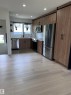 Contemporary kitchen featuring wood-finish cabinetry, stainless steel appliances, a white subway tile backsplash, and light wood-finish flooring - 11911 133 Avenue, Edmonton, AB 