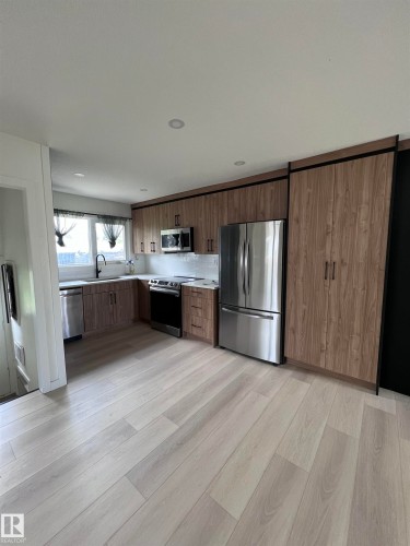 Contemporary kitchen featuring wood-finish cabinetry, stainless steel appliances, white subway tile backsplash, and light wood-finish flooring - 11911 133 Avenue, Edmonton, AB 