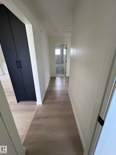 Hallway featuring light wood-finish flooring, white walls, and a black built-in cabinet - 11911 133 Avenue, Edmonton, AB 