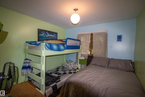 Room featuring light green and light blue walls, wood-finish flooring, a window with horizontal blinds and sheer curtains, and a ceiling-mounted globe light fixture - 104 60201 Rng Rd 122, Rural St. Paul County, AB 