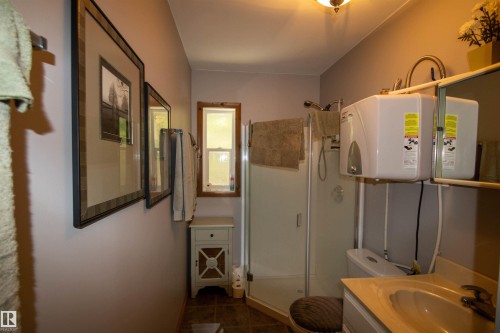 Bathroom featuring a glass-enclosed shower, single vanity with integrated sink, and wall-mounted water heater - 104 60201 Rng Rd 122, Rural St. Paul County, AB 