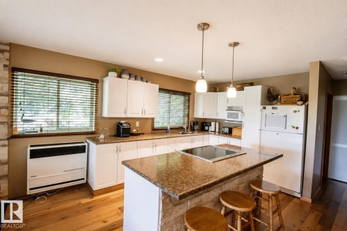 Kitchen featuring white cabinetry, granite-finish countertops, wood-finish flooring, and a central island with a built-in cooktop and pendant lighting - 104 60201 Rng Rd 122, Rural St. Paul County, AB 
