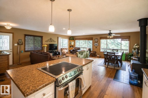 Open-concept living space featuring wood-finish flooring, a kitchen island with integrated cooktop, white cabinetry, and pendant lighting - 104 60201 Rng Rd 122, Rural St. Paul County, AB 