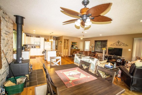 Spacious open-concept interior featuring wood-finish flooring, a modern wood stove with stone-finish wall, a dining area, and a kitchen with white cabinetry and an island - 104 60201 Rng Rd 122, Rural St. Paul County, AB 