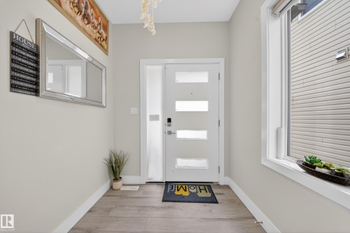 Bright entryway featuring a modern white door with frosted glass inserts, wood-finish flooring, a sidelight, and a large window - 449 Roberts Cres, Leduc, AB 