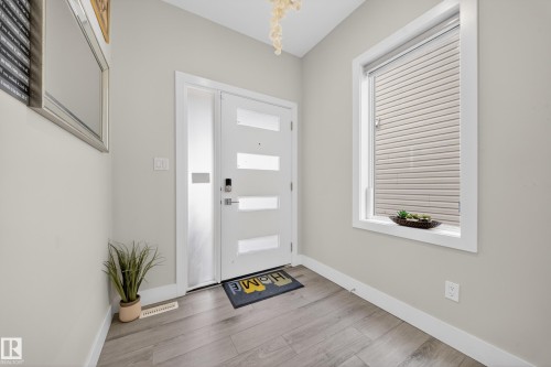 Entryway featuring a modern white door with frosted glass panels, an adjacent full-length frosted glass sidelight, wood-finish flooring, and a large window with white trim - 449 Roberts Cres, Leduc, AB 