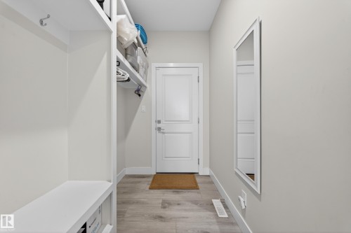 Entryway featuring wood-finish flooring, a full-length wall mirror, built-in storage shelving, a built-in bench, and a panel door - 449 Roberts Cres, Leduc, AB 