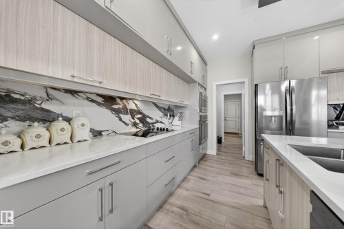 Contemporary kitchen featuring a full-height marble-look slab backsplash, light wood-finish and gray cabinetry, integrated stainless steel appliances, and wood-finish flooring - 449 Roberts Cres, Leduc, AB 